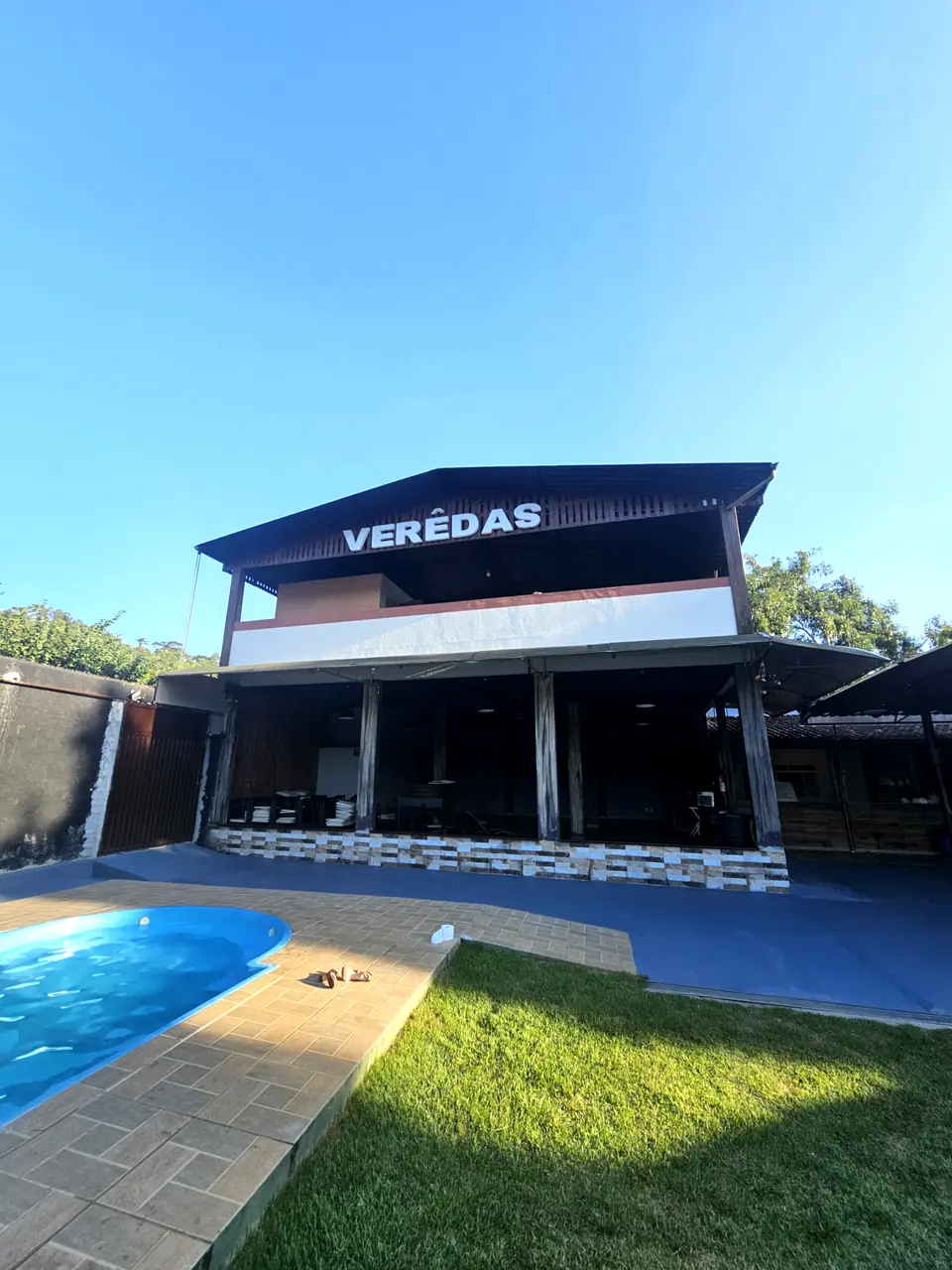 Prédio com o letreiro Verêdas, piscina e gramado em dia de céu azul