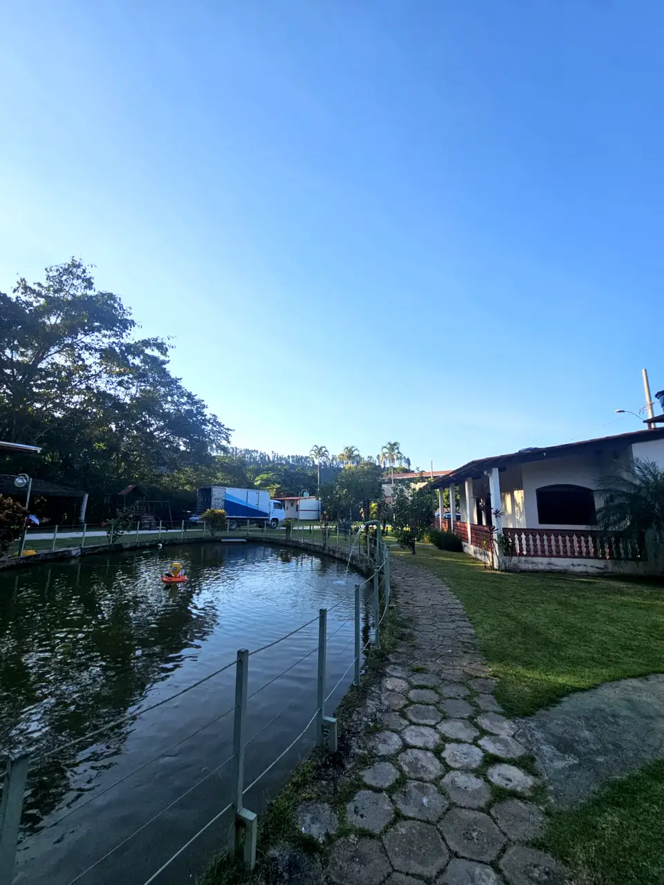 Lago da chácara com caminho de pedras, gramado e árvores