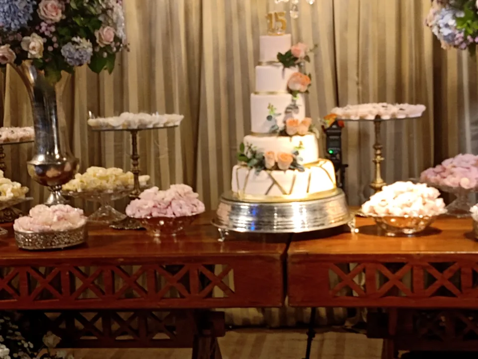 Mesa de doces com bolo de três andares, arranjos de rosas e bandejas de doces