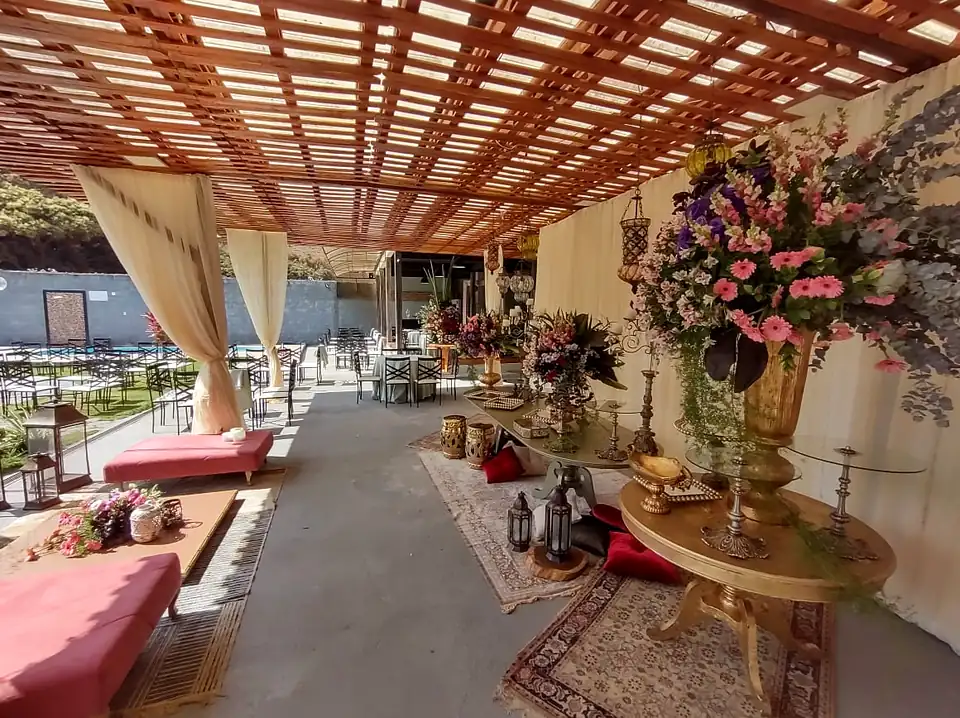 Área coberta decorada para casamento, com arranjos de flores, cortinas brancas e sofás