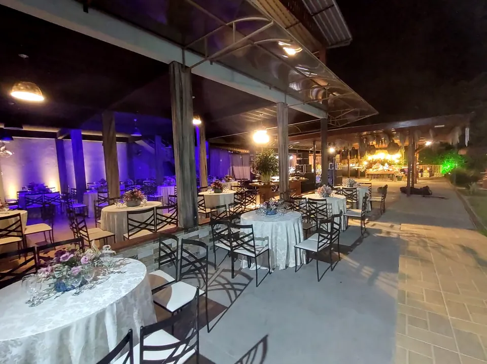 Área de festa à noite com luz azul e roxa e mesas com toalhas brancas